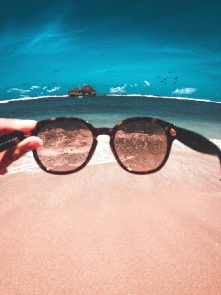 Hand holding sunglasses with a beach and ocean view. Captures summer relaxation vibes.